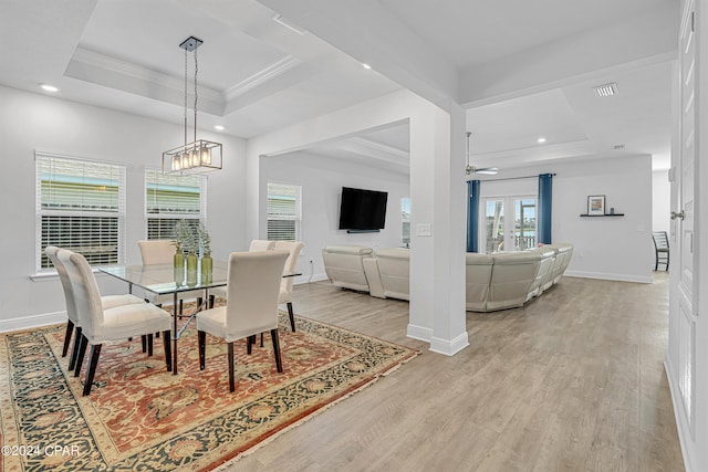 dining area with ceiling fan with notable chandelier, a raised ceiling, light wood-type flooring, and ornamental molding