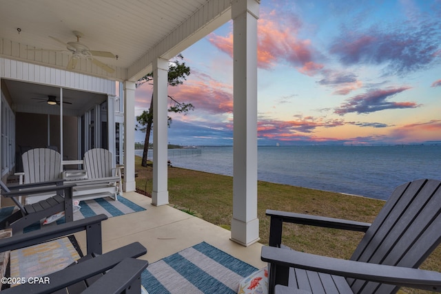 patio terrace at dusk with a lawn, ceiling fan, and a water view