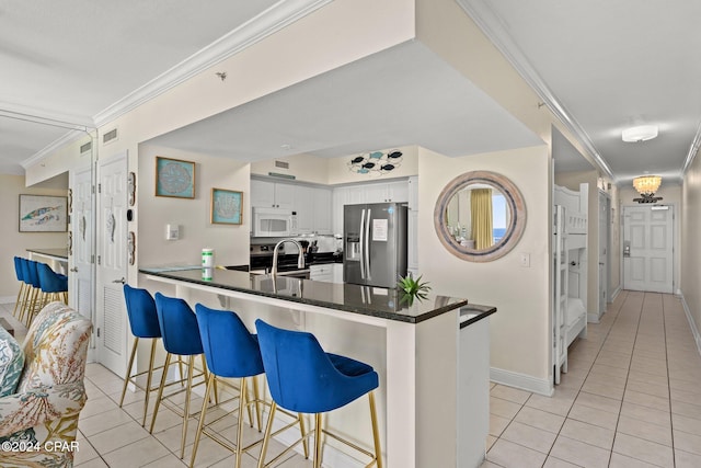 kitchen featuring stainless steel refrigerator with ice dispenser, kitchen peninsula, crown molding, a kitchen bar, and white cabinets