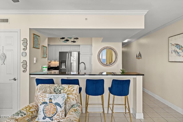 kitchen with white cabinets, stainless steel refrigerator with ice dispenser, a breakfast bar area, light tile patterned floors, and ornamental molding