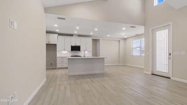 kitchen featuring white cabinets, an island with sink, high vaulted ceiling, and light hardwood / wood-style flooring