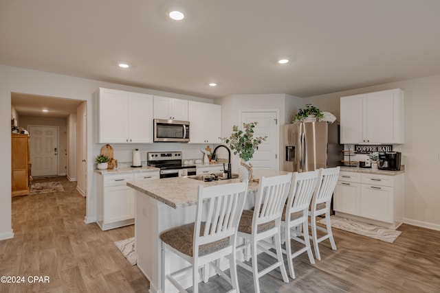 kitchen with a kitchen island with sink, stainless steel appliances, sink, white cabinetry, and light hardwood / wood-style floors