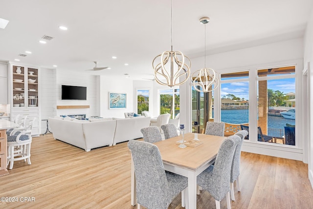 dining room with light hardwood / wood-style floors, a fireplace, ceiling fan with notable chandelier, and plenty of natural light