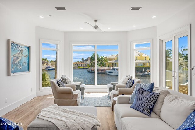 living room featuring a wealth of natural light, light hardwood / wood-style flooring, a water view, and ceiling fan