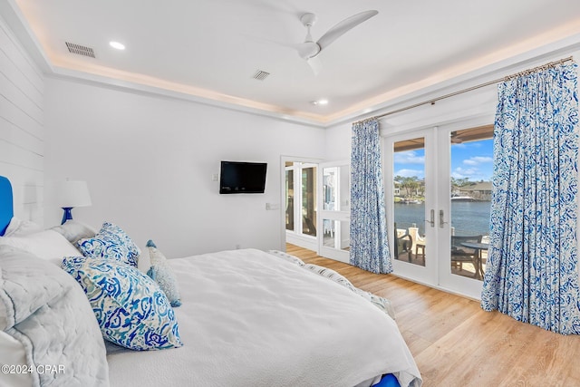 bedroom with french doors, access to exterior, a tray ceiling, hardwood / wood-style floors, and ceiling fan