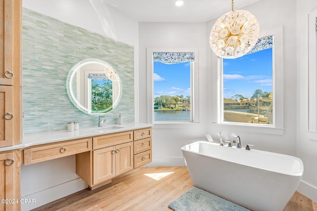 bathroom featuring a bathtub, wood-type flooring, a notable chandelier, vanity, and a water view