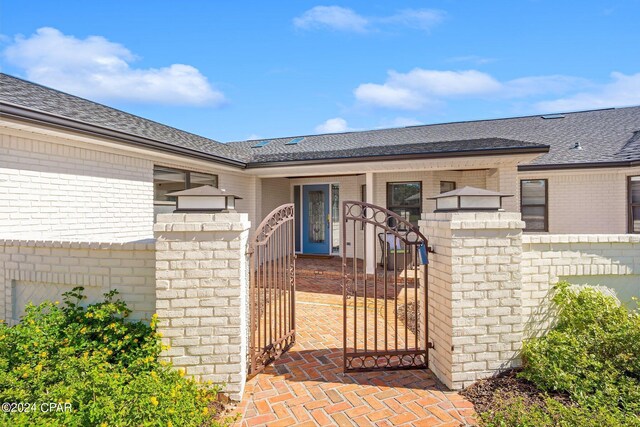 443 Wahoo Rd, Panama City Beach, FL 32408 - view of exterior entry featuring brick siding, a gate, fence, and a shingled roof
