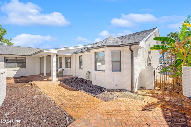 443 Wahoo Rd, Panama City Beach, FL 32408 - view of front facade with brick siding, a gate, a shingled roof, and a patio area