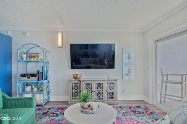 living area with crown molding, a textured ceiling, baseboards, and wood finished floors