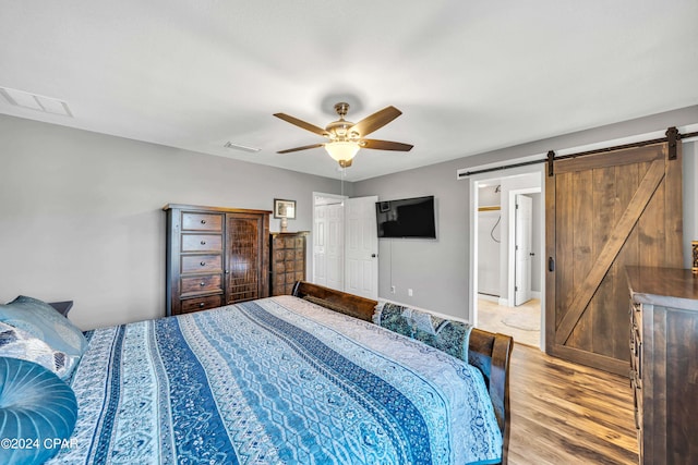 bedroom with a barn door, ceiling fan, and light wood-type flooring