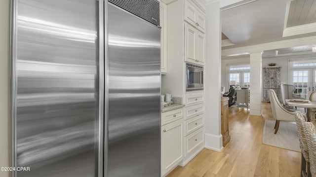 kitchen with light stone countertops, crown molding, light wood finished floors, built in appliances, and ornate columns