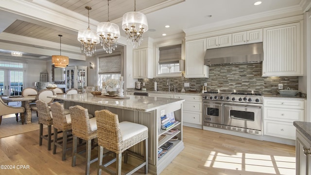 kitchen with decorative backsplash, double oven range, under cabinet range hood, and a sink