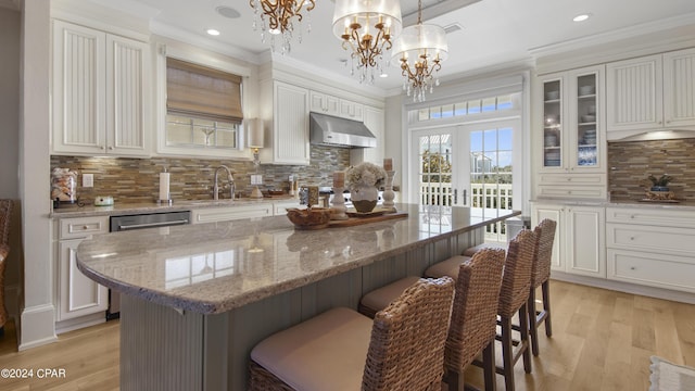 kitchen featuring light wood-style flooring, a sink, ornamental molding, under cabinet range hood, and dishwasher