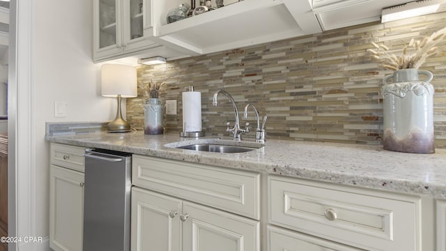 kitchen with tasteful backsplash, glass insert cabinets, light stone counters, white cabinets, and a sink