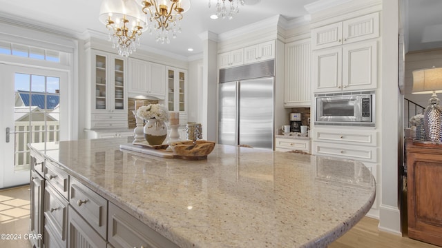 kitchen featuring ornamental molding, a center island, white cabinets, built in appliances, and light stone countertops