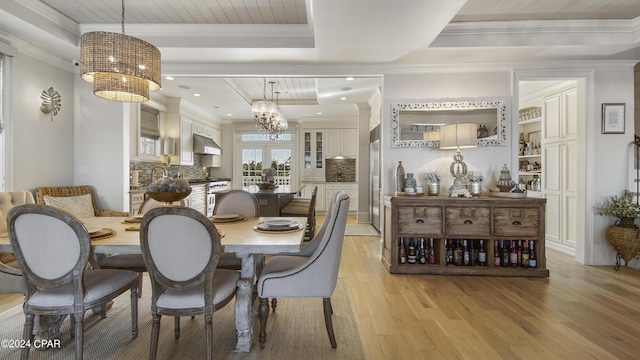 dining room featuring a chandelier, light wood-style flooring, a raised ceiling, and ornamental molding