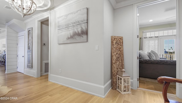 hall with visible vents, baseboards, light wood finished floors, an inviting chandelier, and crown molding