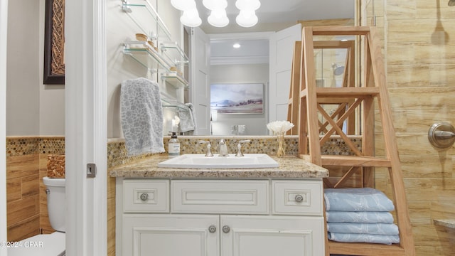 bathroom with a wainscoted wall, toilet, tile walls, and vanity