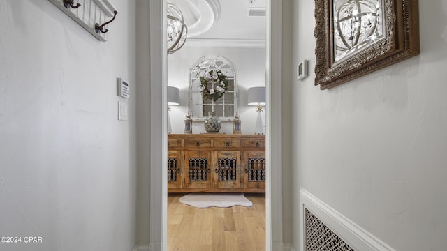 hallway featuring wood finished floors, visible vents, and ornamental molding