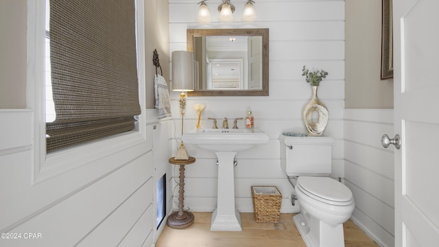 half bath with toilet, wood finished floors, and a sink