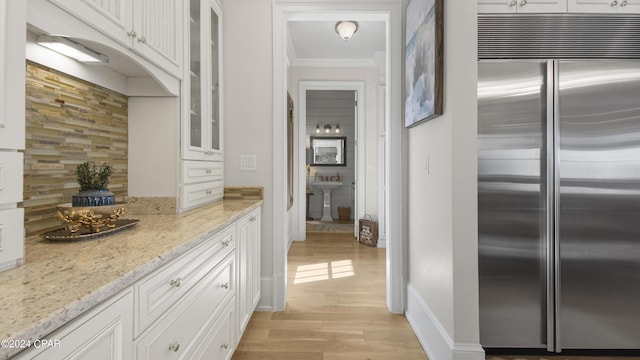 kitchen with light stone counters, stainless steel built in fridge, glass insert cabinets, white cabinetry, and crown molding