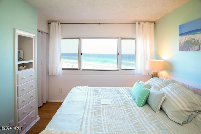 bedroom with a textured ceiling, hardwood / wood-style flooring, and a water view