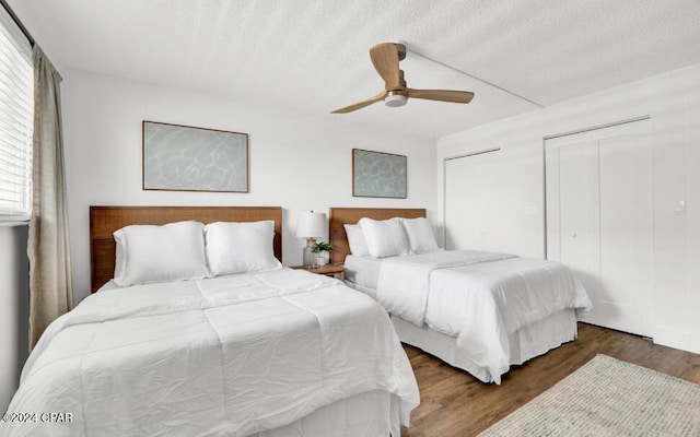 bedroom featuring ceiling fan, a textured ceiling, multiple closets, and dark hardwood / wood-style flooring