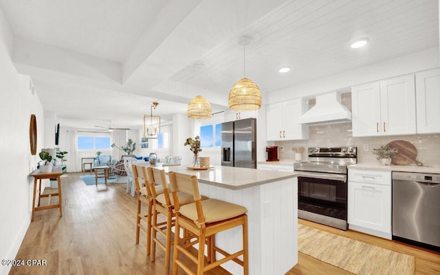 kitchen featuring appliances with stainless steel finishes, a kitchen island, white cabinetry, custom exhaust hood, and light hardwood / wood-style flooring