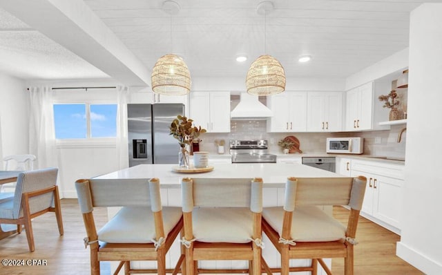 kitchen with pendant lighting, stainless steel appliances, white cabinetry, and premium range hood