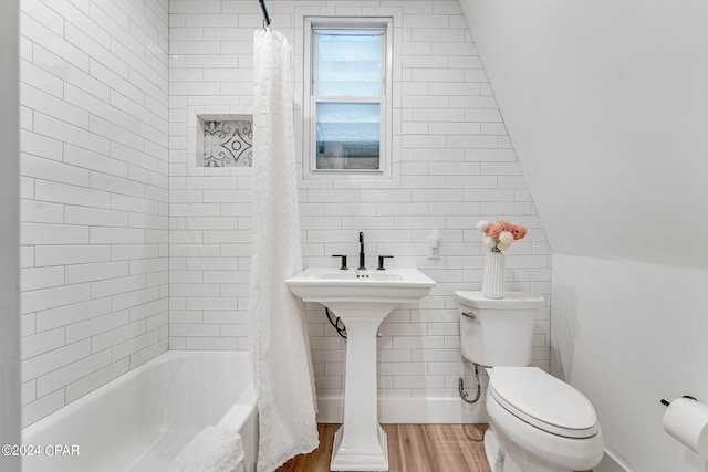 bathroom with lofted ceiling, shower / bathtub combination with curtain, wood-type flooring, tile walls, and toilet