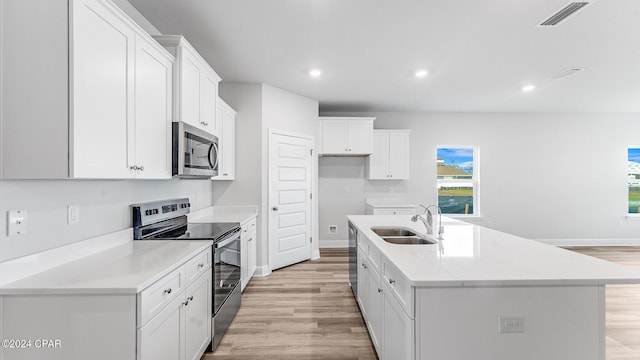 kitchen featuring white cabinets, sink, light wood-type flooring, an island with sink, and stainless steel appliances