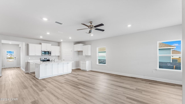 kitchen with a kitchen island with sink, light hardwood / wood-style flooring, ceiling fan, appliances with stainless steel finishes, and white cabinetry