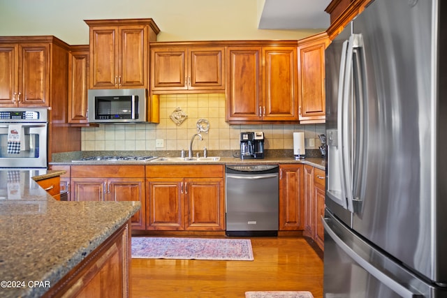 kitchen with decorative backsplash, appliances with stainless steel finishes, sink, stone countertops, and light hardwood / wood-style floors