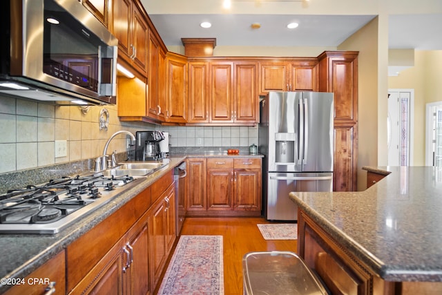 kitchen with sink, tasteful backsplash, dark stone countertops, appliances with stainless steel finishes, and light wood-type flooring