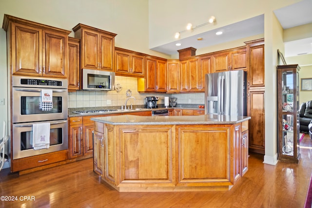 kitchen with hardwood / wood-style floors, a center island, backsplash, light stone counters, and stainless steel appliances