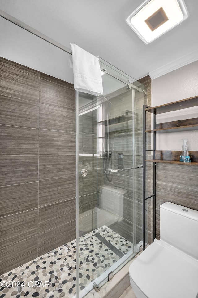 bathroom featuring a shower with door, ornamental molding, and toilet