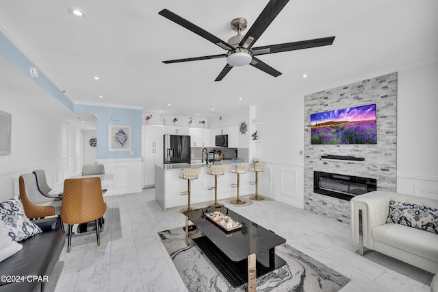 living room featuring crown molding, sink, ceiling fan, and a fireplace