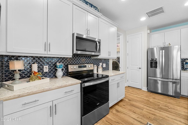 kitchen featuring white cabinets, stainless steel appliances, light wood-type flooring, and tasteful backsplash