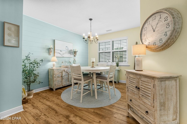 dining area with hardwood / wood-style flooring, an inviting chandelier, and wooden walls