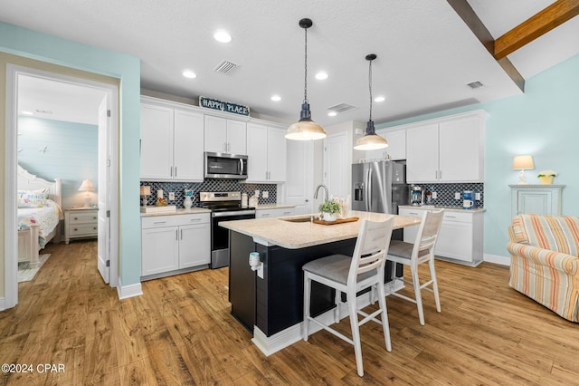 kitchen with stainless steel appliances, a center island with sink, white cabinetry, and hanging light fixtures