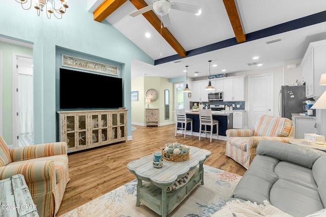 living room with ceiling fan with notable chandelier, light hardwood / wood-style floors, and vaulted ceiling with beams