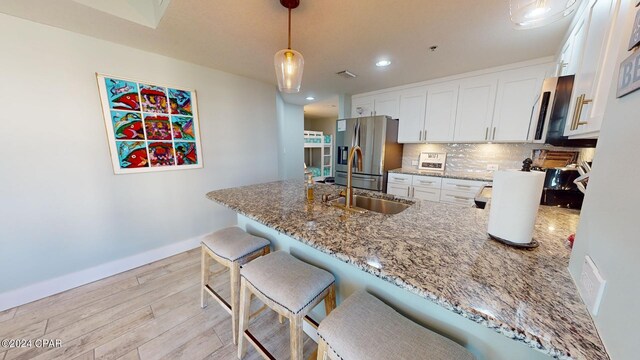 kitchen featuring light stone countertops, stainless steel fridge, white cabinetry, pendant lighting, and light hardwood / wood-style flooring