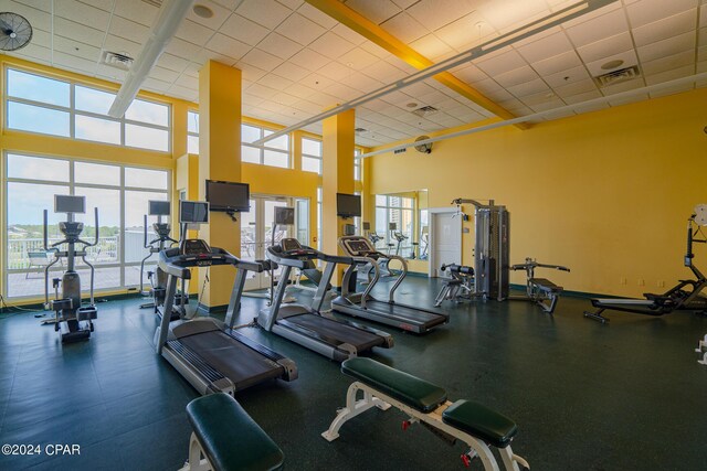 gym featuring a drop ceiling, a healthy amount of sunlight, and a high ceiling