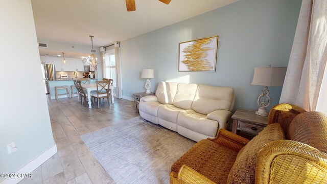 living room with light hardwood / wood-style floors and ceiling fan with notable chandelier