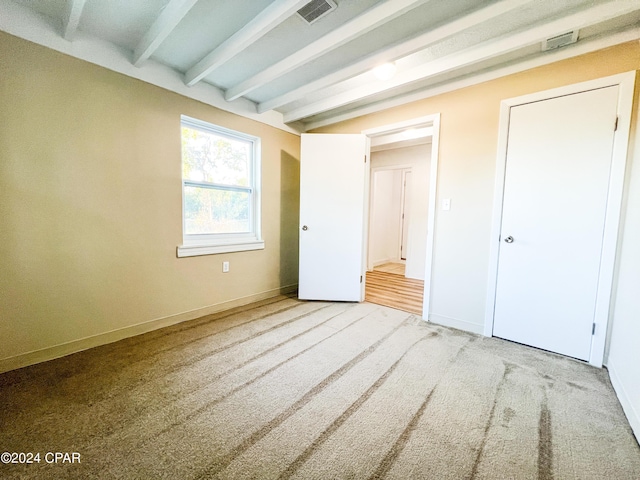 unfurnished bedroom with beam ceiling and carpet flooring