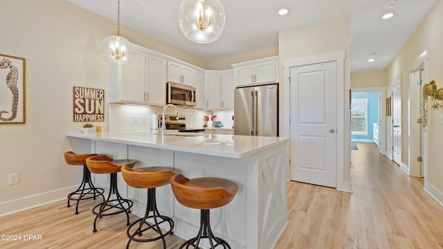 kitchen with kitchen peninsula, light hardwood / wood-style flooring, appliances with stainless steel finishes, decorative light fixtures, and white cabinetry