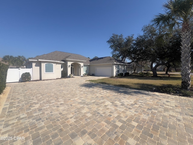 view of front facade with an attached garage, fence, decorative driveway, and stucco siding