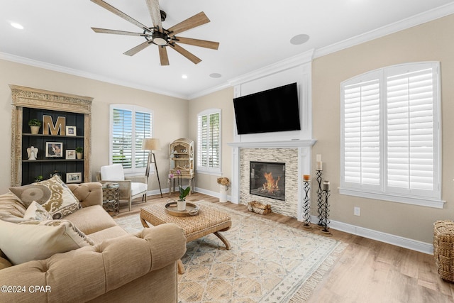 living area featuring light wood-type flooring, baseboards, ornamental molding, and a glass covered fireplace