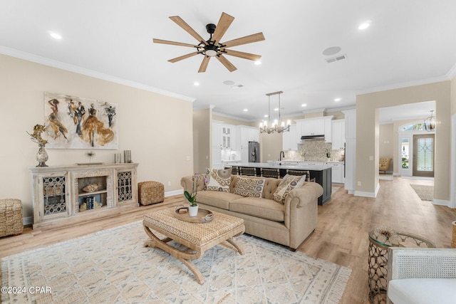 living room featuring ceiling fan with notable chandelier, visible vents, baseboards, ornamental molding, and light wood finished floors