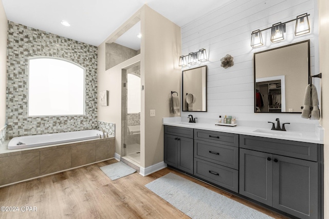 full bath featuring double vanity, a stall shower, a sink, wood finished floors, and a bath